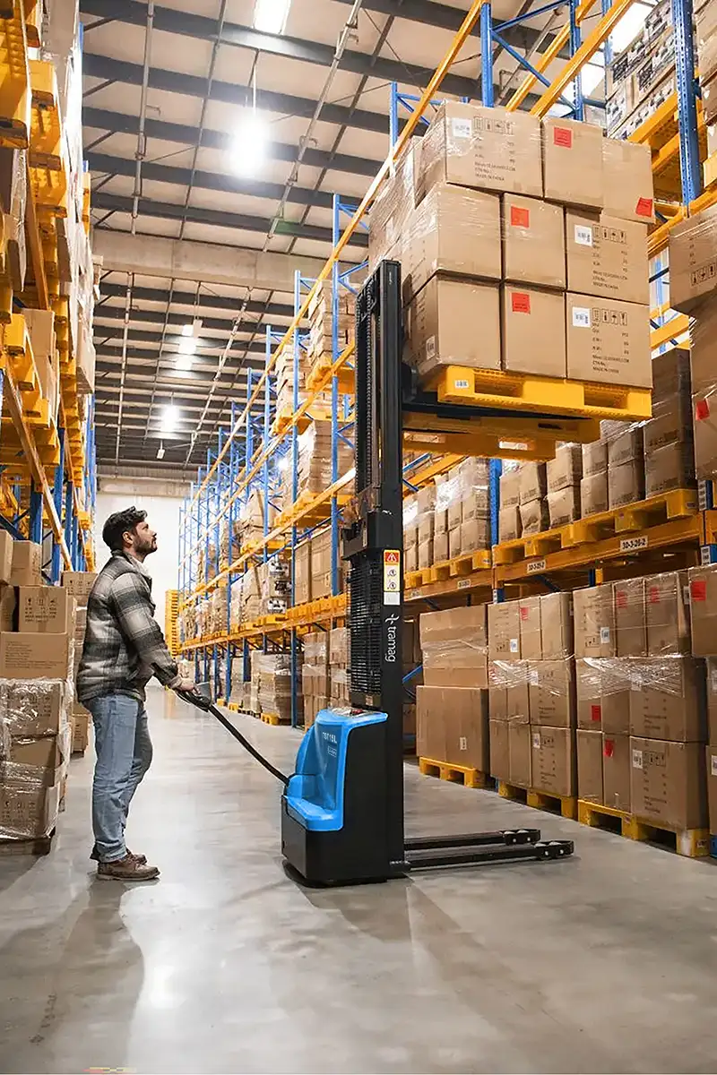 Tramag TST15L elektrische stapelaar met lithium-ion accu tijdens het verplaatsen van pallets in een magazijnomgeving.
