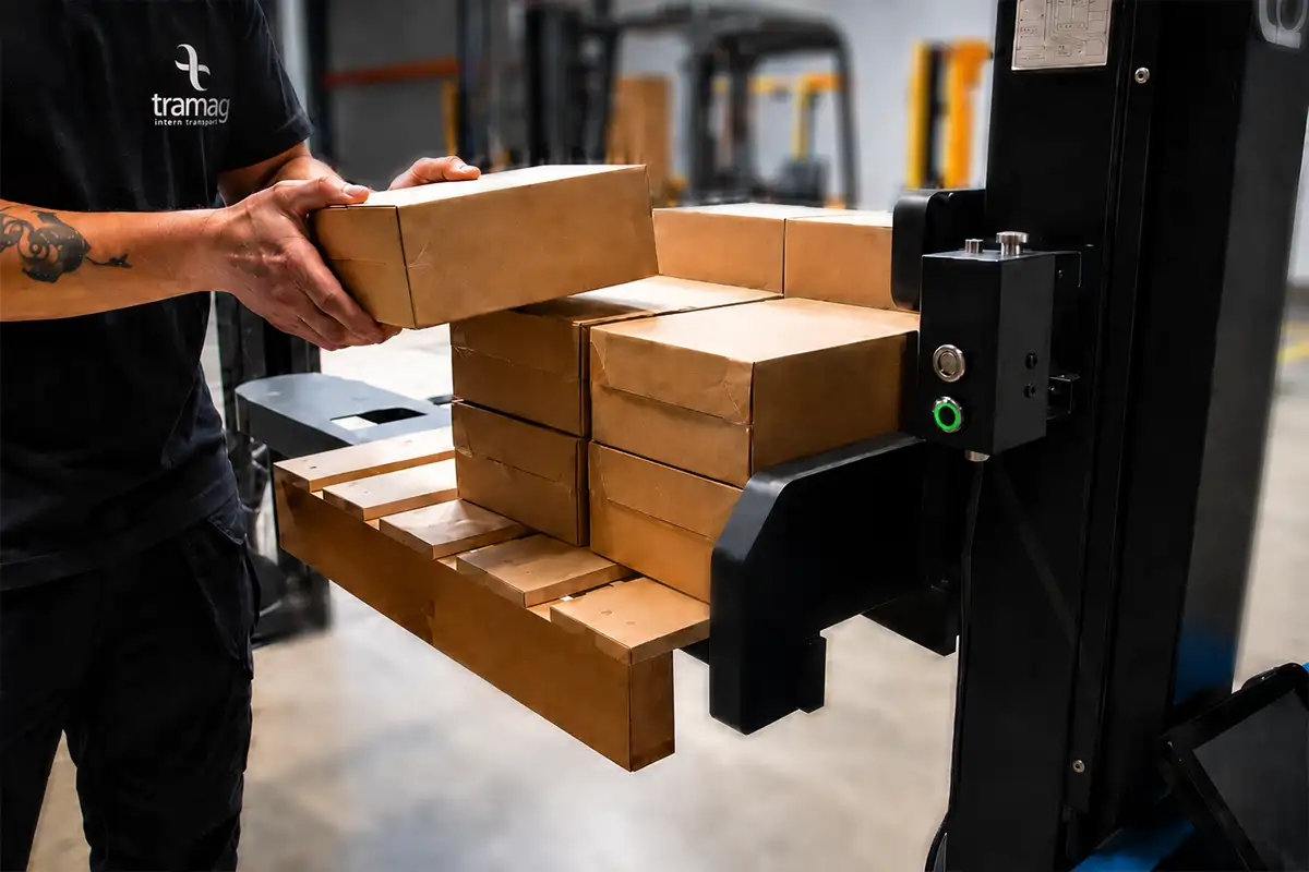 Collega plaatst dozen op een pallet met de TSAH12-M stapelaar, terwijl de automatische hoogteregeling de vorken op ergonomische werkhoogte houdt.